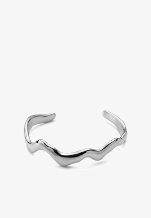 Sølvfarget metallarmbånd med glatt, uregelmessig bølget design og åpne ender, vist på en hvit overflate.