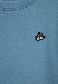 Hanorac albastru dintr-un amestec neted de bumbac, cu un emblemă cusută a unei păsări albe cu contur negru pe pieptul stâng.