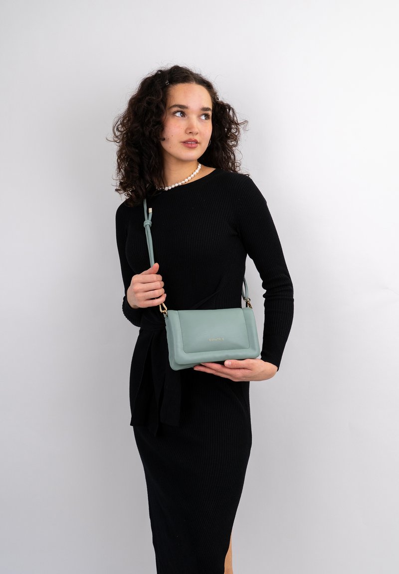 Borsa a tracolla in cuoio verde menta con superficie liscia, dettagli in metallo dorato e tracolla annodata removibile. Design compatto.