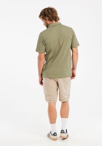 Olijfgroen polo shirt met korte mouwen, beige shorts, witte sokken en zwarte sportschoenen. Eenvoudig design, comfortabele pasvorm en natuurlijke stoftextuur.