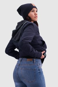 Marineblaue Bomberjacke aus strukturiertem Stoff, mit einer hinterhängenden Kapuze, kombiniert mit hellblauen Jeans. Schwarze Mütze mit einem Labelakzent.