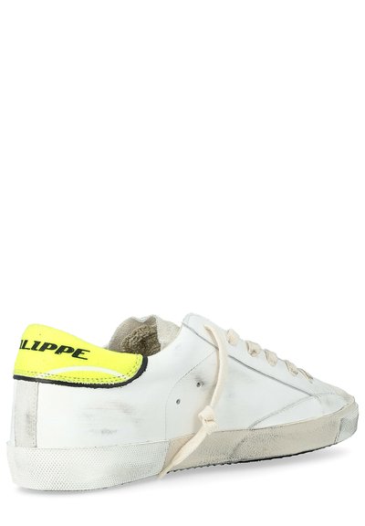 Sneaker bianco a scarpa bassa con suola consumata, lacci beige annodati e un tallone giallo brillante etichettato "PHILIPPE".