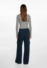 Harmaa ribattua pitkähihasta toppia yhdistettynä leveälahkeisiin tummansinisiin cargo-housuihin, joissa on sivutaskut ja joustava vyötärö.