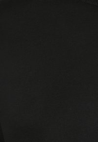 Närbild av svart texturerad tyg med fint stickat mönster, som visar detalj av material och väv.