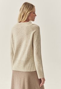 Beige kötött pulóver bordás aljjal és mandzsettával, finoman foltos textúrával, hátulról mutatva, kerek nyakkivágással.