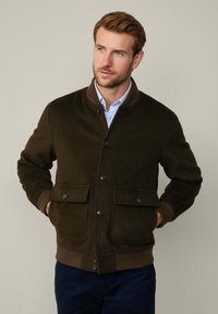 Dark green wool-blend jacket with a round collar, front button closure, two flapped pockets, and ribbed hem and cuffs.
