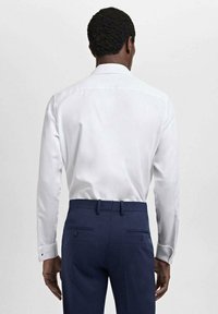 Witte langearmige shirt met een getailleerde pasvorm en knoopmanchetten, gecombineerd met marineblauwe broek met een gladde textuur en discrete achterzakken.