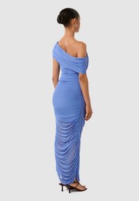 Dlhý modrý šatový model s off-shoulder strihom, jemnou textúrou a priliehavým strihom, doplnený o sandále na opätku s remienkami.