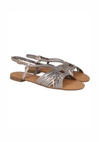 Sandalias metálicas plateadas con diseño trenzado y suela plana. Presentan un empeine con tiras y una hebilla en el tobillo para un ajuste ajustable.