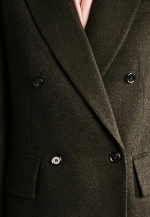 Double-breasted olive green blazer with a textured wool finish, black buttons, and notched lapels, featuring two front pockets.