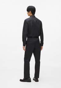 Melna ilga piedurkne krekls ar norādītu apkakli un pogu detaļām, apvienots ar melniem biksēm. Abiem izstrādājumiem ir eleganta, gluda tekstūra.