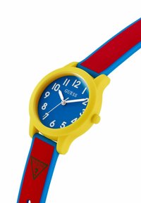 Montre en silicone colorée avec un boîtier rond jaune, un cadran bleu, des chiffres blancs et un bracelet multicolore rouge et bleu. Présente un logo triangulaire.