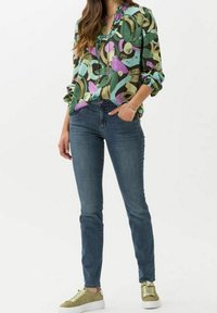 Grön och lila mönstrad blus med volangkrage, kombinerad med mörkblå figurnära jeans och ljusgröna sneakers.