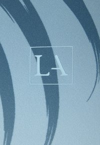 Lichtblauwe stof met donkerblauwe kwaststreken en een geborduurd "LA" binnen een gestikt vierkantomtrek.