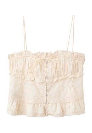 Crop top sans manches couleur crème avec bords froncés, fines bretelles, boutons sur le devant, nœud papillon au niveau de la poitrine et détails en dentelle.