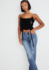 Black knitted crop top with adjustable ties, featuring a textured pattern and silver chain straps; paired with light blue, distressed denim jeans.