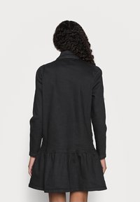 Černé šaty s dlouhými rukávy a rozšířeným spodním lemem. Vyrobeny z měkké látky s jednoduchým designem, s límcem a nařaseným pasem.