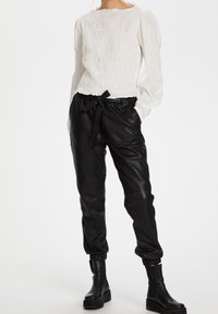 Haut blanc à manches longues smocké, associé à un jogger en cuir noir avec une taille élastique et un nœud. Des bottines noires à plateforme complètent la tenue.