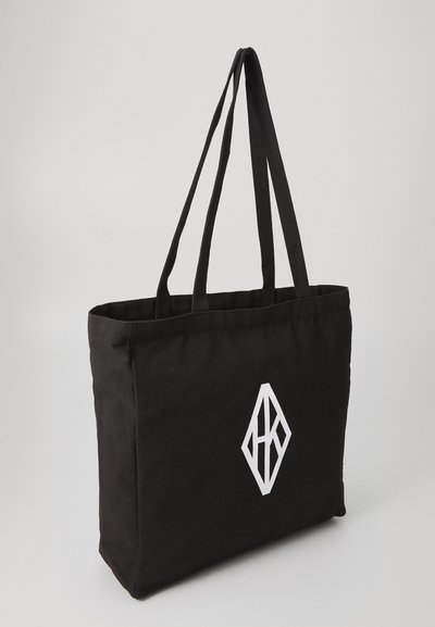 Črna platnena torba z dvema naramnicama, ki na eni strani nosi bel geometrijski logotip. Enostavna oblika in trden material.