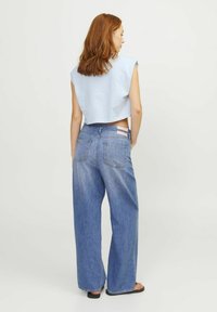 Top corto azul claro con mangas cortas, combinado con unos vaqueros de mezclilla azules de tiro alto y pierna ancha, que cuentan con dos bolsillos traseros y costuras mínimas.