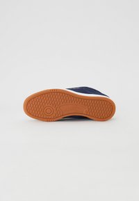 Navy sneaker with a textured rubber sole in orange and white, featuring a smooth upper design and a prominent Reebok logo on the sole.