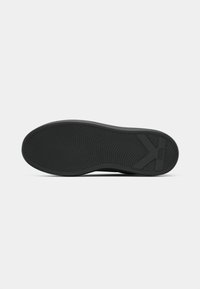 Suela de zapato de goma negra con un patrón ondulado. Presenta un soporte para el talón prominente y un logo. Textura suave, bordes redondeados y un diseño plano.
