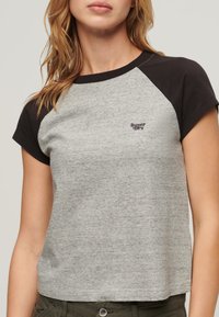 Szara koszulka z krótkim rękawem z heather z czarnymi rękawami raglanowymi, z małym logo "Superdry" na piersi. Miękka faktura i luźny krój.