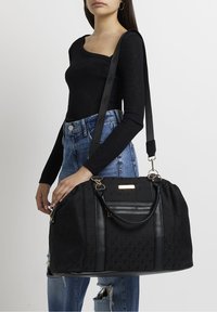 Sac noir avec un tissu texturé, des accents en cuir et du matériel doré. Présente une bandoulière détachable et une poche zippée. Forme arrondie.