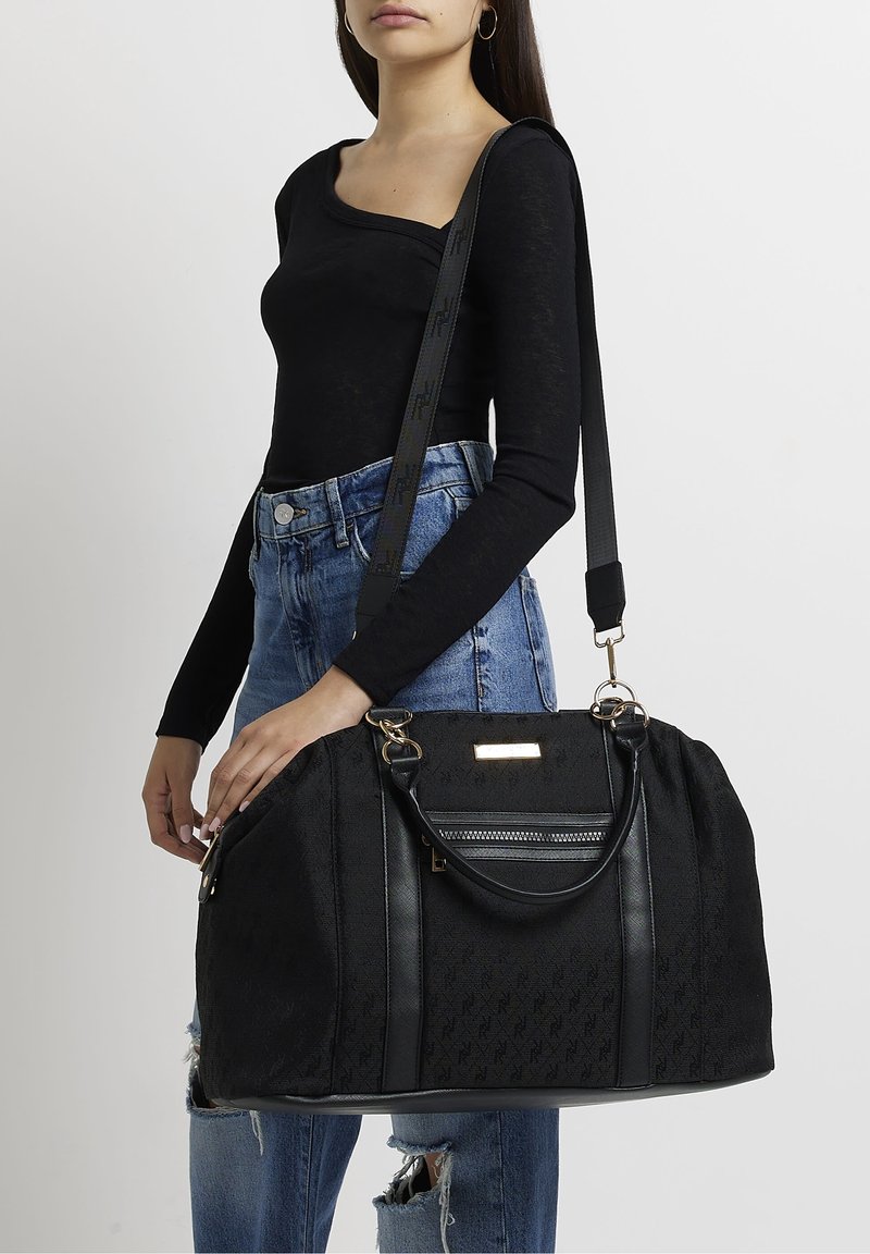 Sac noir avec un tissu texturé, des accents en cuir et du matériel doré. Présente une bandoulière détachable et une poche zippée. Forme arrondie.