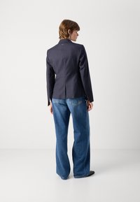 Tmavý pruhovaný blazer má tailored střih, jeden rozvent v zadní části a je spojen s širokými modrými denimovými džíny.