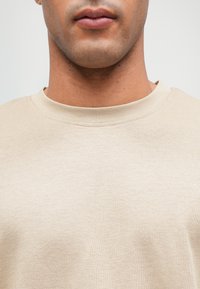 Beige crew neck sweatshirt made of soft fabric, featuring a smooth texture and a simple design, highlighting a relaxed fit and minimal stitching.
