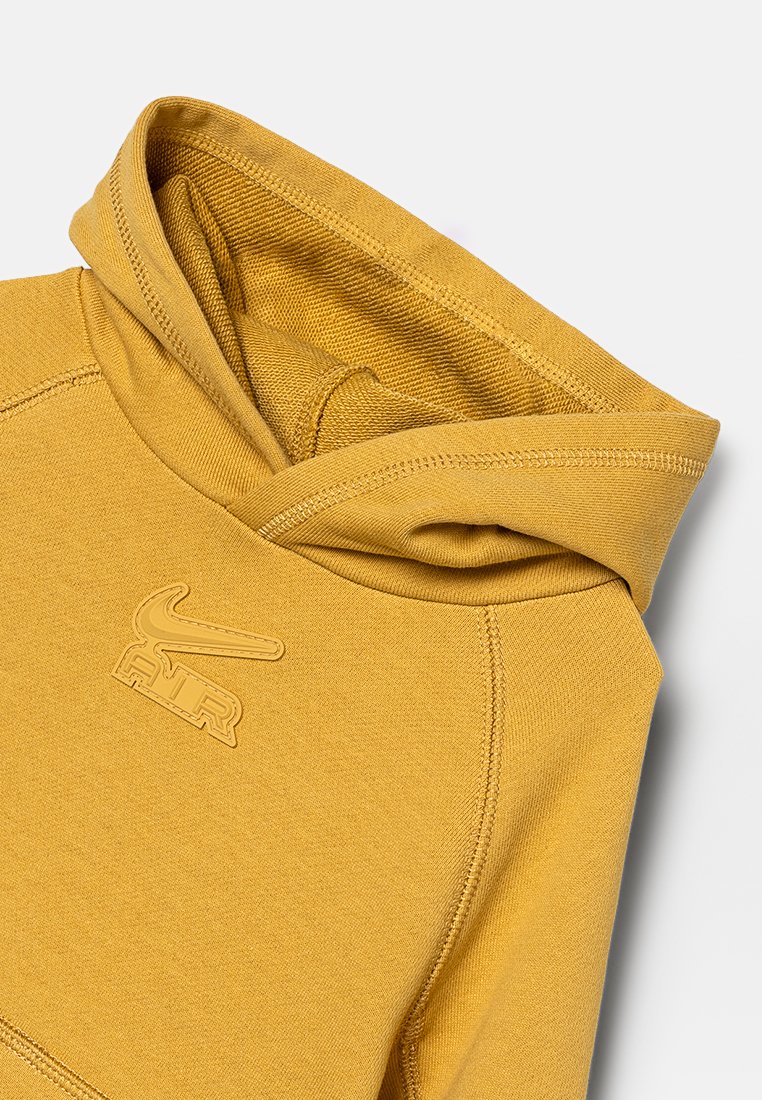 Hoodie jaune moutarde avec des coutures cousues et un logo Nike Air embossé sur la poitrine, montrant la capuche repliée et la texture du tissu.
