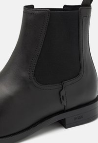 Black leather Chelsea boot featuring elastic side panels, a smooth finish, and a low block heel. Subtle stitching and brand logo detail.