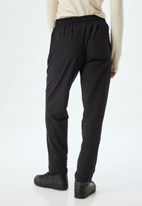 Sorte, lette, strækbare bukser med elastisk talje og taperede ben. De er parret med sorte, strukturerede sneakers.