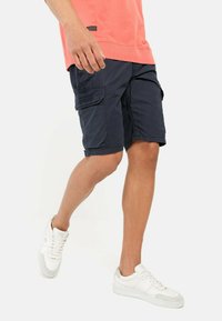 Navy cargoshorts met meerdere zakken, gemaakt van lichtgewicht stof, met een relaxte fit en een verstelbare tailleband. Draagt met witte sneakers.