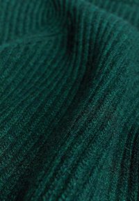 Tissu côtelé vert foncé avec une apparence épaisse et texturée, présentant des variations subtiles de couleur et de fibres visibles à la surface.