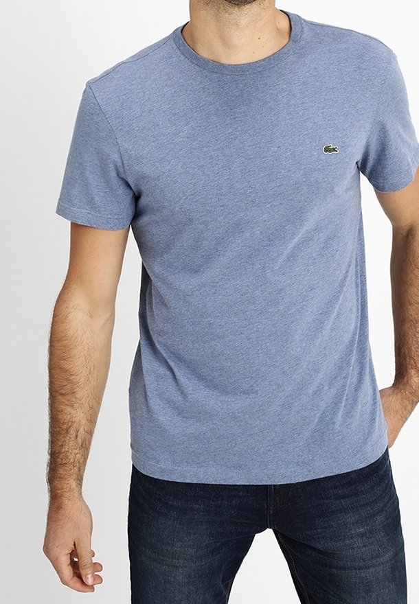 Light blue cotton t-shirt with a crew neck, short sleeves, and a small green crocodile emblem on the left chest. Worn with dark jeans.