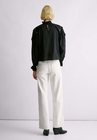 Blusa nera con maniche a balze e dettagli in pizzo; particolare con apertura a chiave sul retro. Abbinata a jeans bianchi a gamba dritta e scarpe verde con tacco.