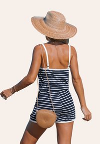 Romper à rayures bleu marine et blanches avec bretelles ajustables, associé à un sac rond en paille tissée. Avec une texture lisse et un design décontracté.