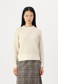 Maglione lavorato a maglia color crema con colletto e polsini a costine. Presenta un motivo testurizzato e una vestibilità leggermente rilassata, abbinato a una gonna scozzese.