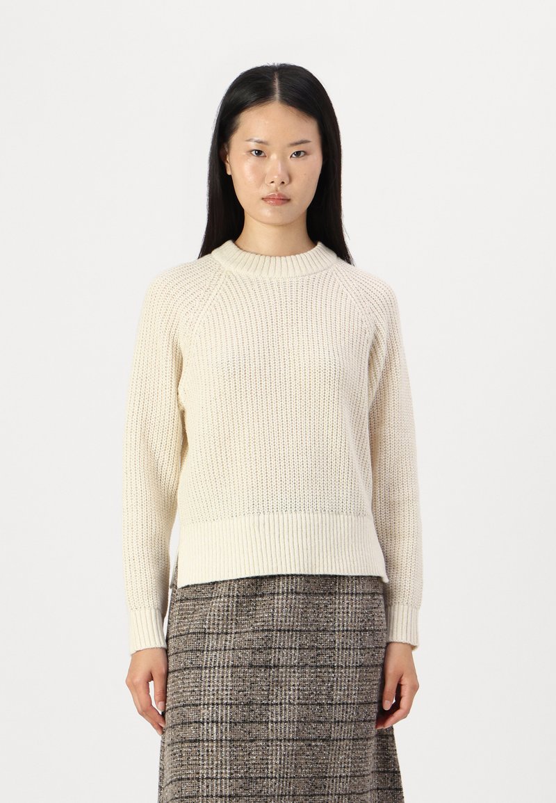 Maglione lavorato a maglia color crema con colletto e polsini a costine. Presenta un motivo testurizzato e una vestibilità leggermente rilassata, abbinato a una gonna scozzese.