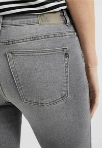 Sivé džíny z denimu s vysokým pasem, představující zadní kapsu a štítek označený "BLUE RIDGE". Viditelné švy v jasnějším tónu.