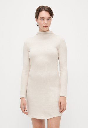 Robe en maille côtelée couleur beige clair, avec des manches longues et un col haut. L'ourlet est légèrement arrondi, mettant en valeur une silhouette ajustée.