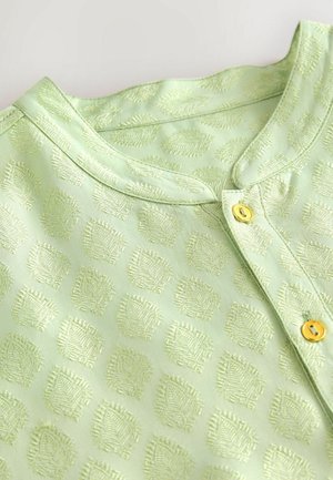 Hellgrüne Bluse mit einem strukturierten Muster aus kleinen Quadraten mit diagonalen Linien, ergänzt durch goldene Knöpfe und einen runden Ausschnitt.
