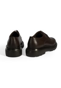 Braune Lederschuhe mit abgerundeten Zehen, glatter Oberfläche und dicken, schwarzen Gummisohlen. Sie verfügen über minimale Nähte und ein klassisches Schnürdesign.