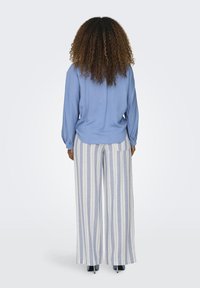 Světle modrá halenka s dlouhým rukávem v kombinaci se širokými pruhovanými kalhotami v modré a bílé. Outfit má uvolněný střih a jemnou texturu.