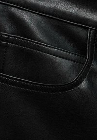 Tela de cuero negro que muestra un primer plano detallado de la textura, la costura y un bolsillo trasero. El material parece suave con un ligero brillo.