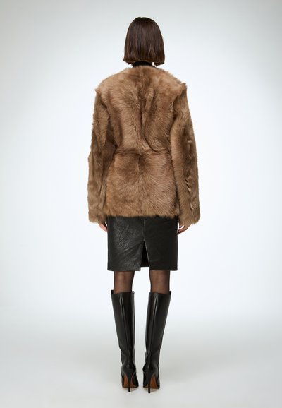 Cappotto in ecopelliccia marrone con una vestibilità comoda, abbinato a una gonna a matita in pelle nera e stivali neri con tacco a spillo al ginocchio.