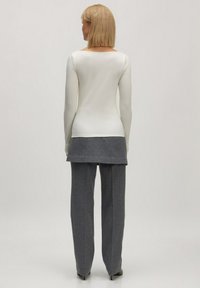 Witte longsleeve top met een lage rug, gecombineerd met losse grijze broeken. Vlekkeloze textuur, neutrale kleuren, eenvoudig ontwerp.
