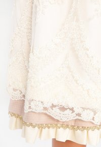 Tissu en dentelle crème avec broderie florale sur les bords froncés rose et crème de la jupe avec bordure dorée.
